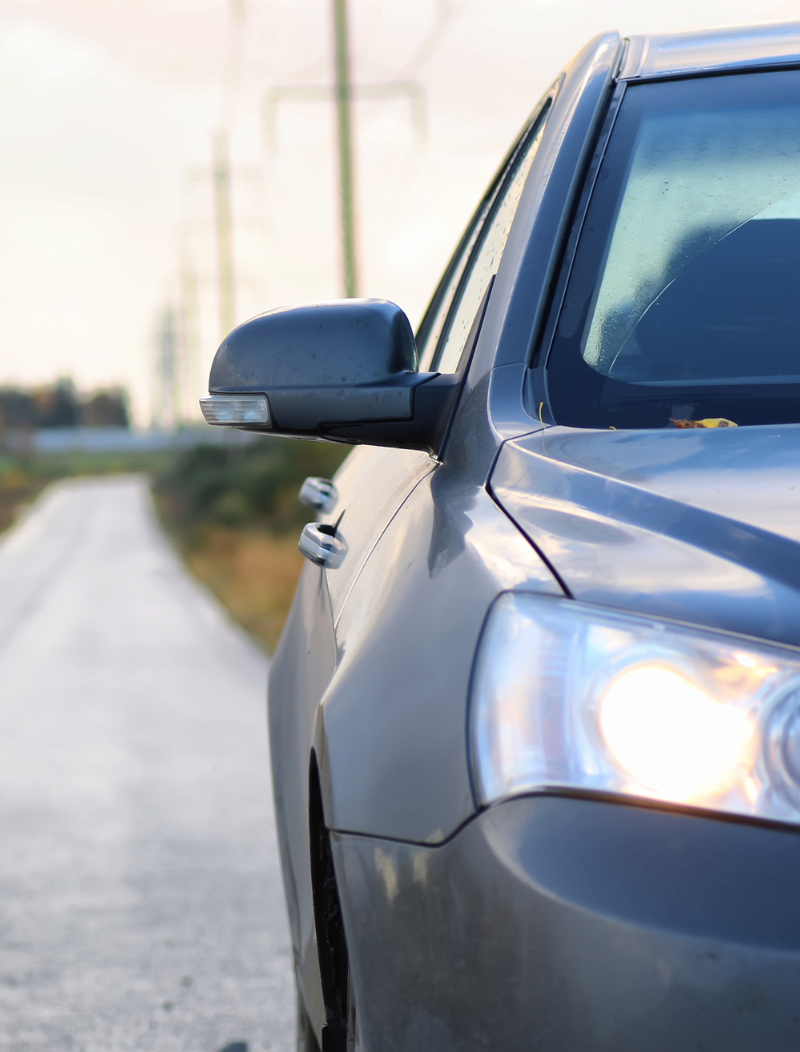 Grey car with headlights on, parked on rural road