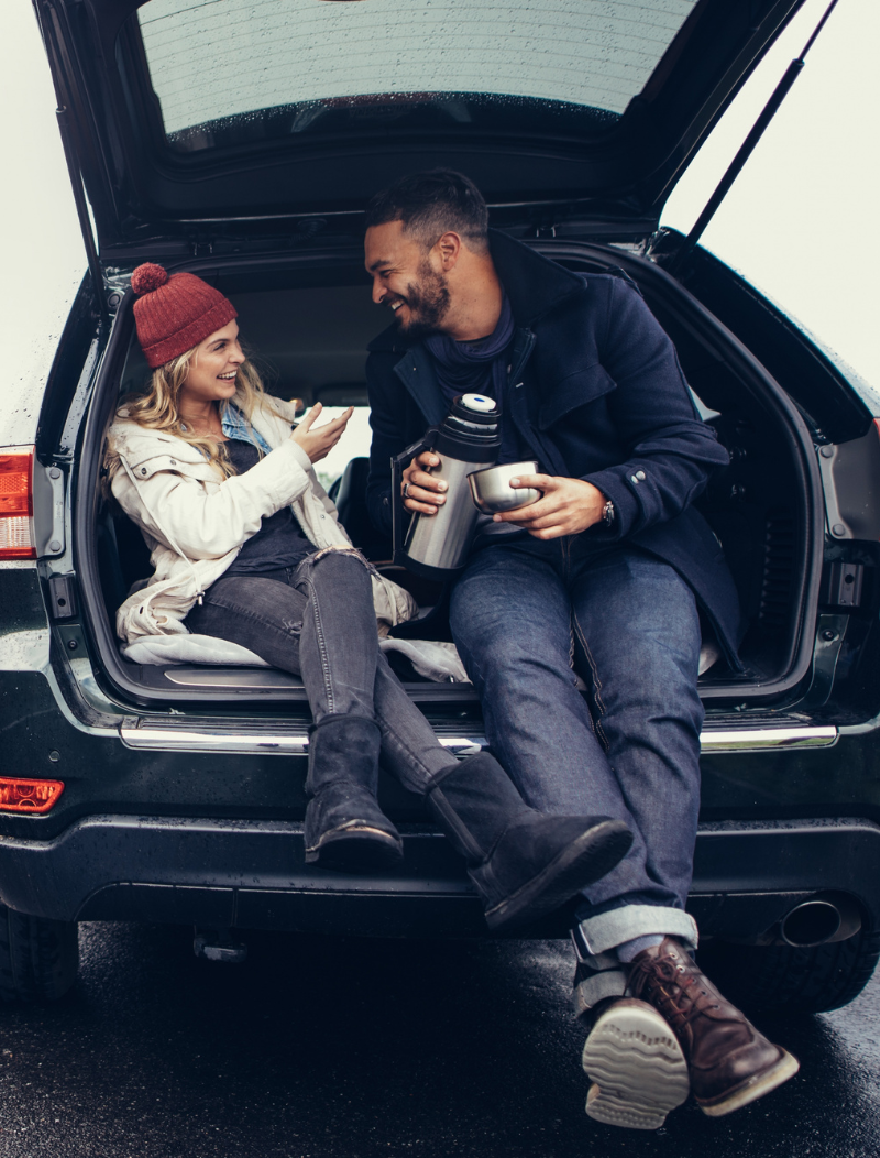 Young couple sat in car boot by side of the road