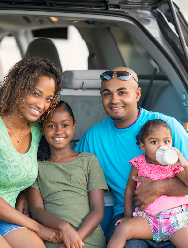 Young family sat looking out of the boot of a car