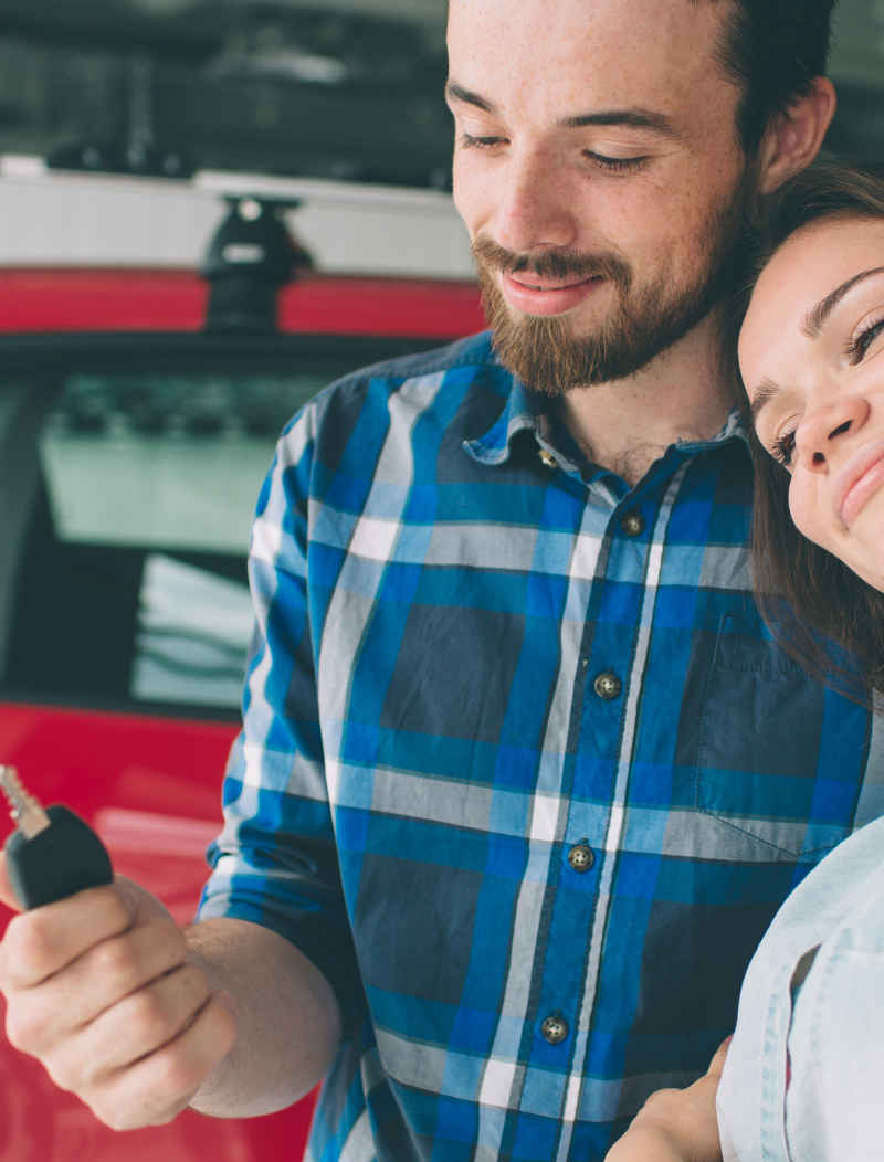 Man holding key of new car with attractive woman leaning on his shoulder