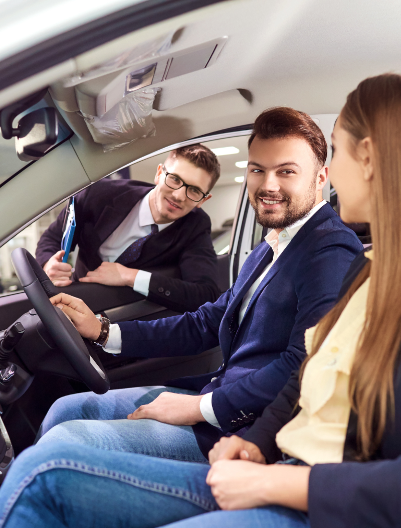 Young couple sat in new car while salesman leans through window
