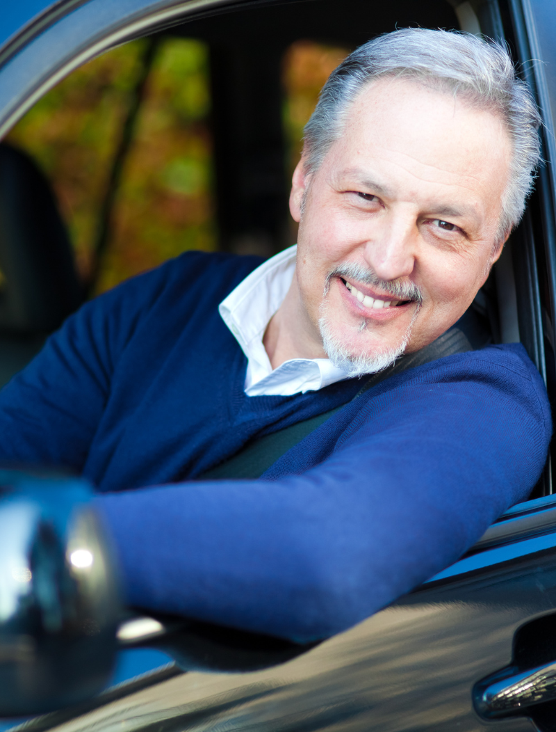 Older motorist smiling while leaning out of car window