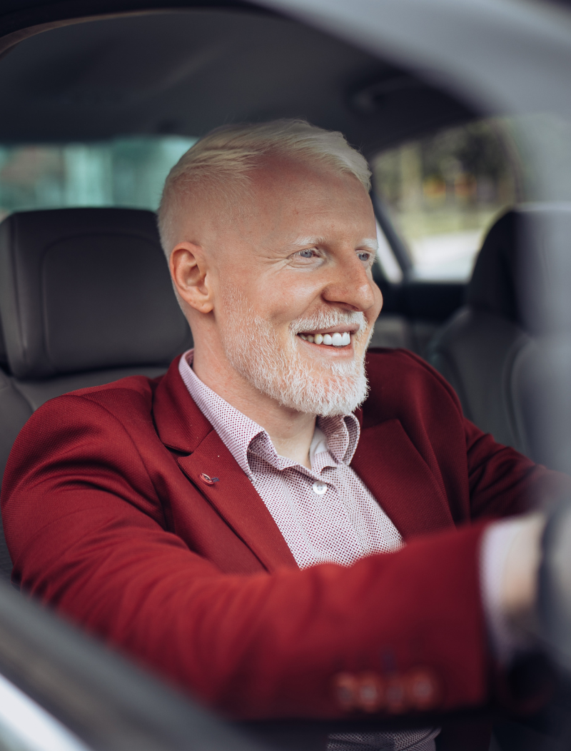 Middle aged man in red blazer driving car