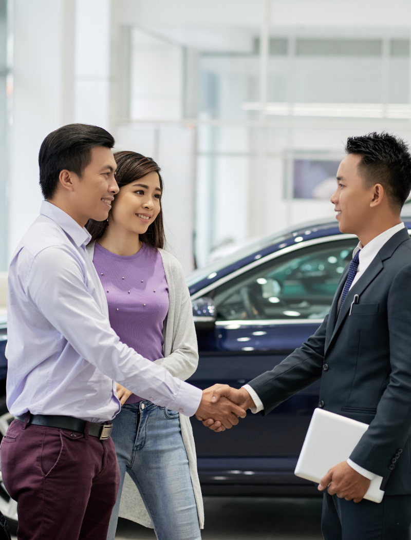 Asian couple shaking hands with car salesman