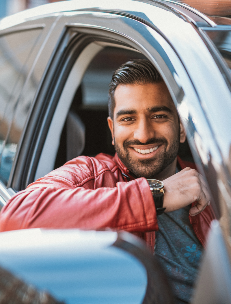 Smiling man in red leather jacket resting arm on car window
